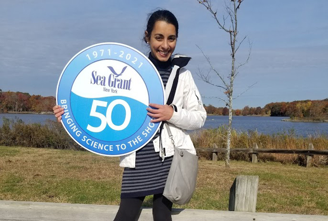 NYSG's Long Island Sound Study Outreach Coordinator Lillit Genovesiat is pictured holding a Sea Grant 50 year anniversary poster in front of the Edith G. Read Wildlife Sanctuary.